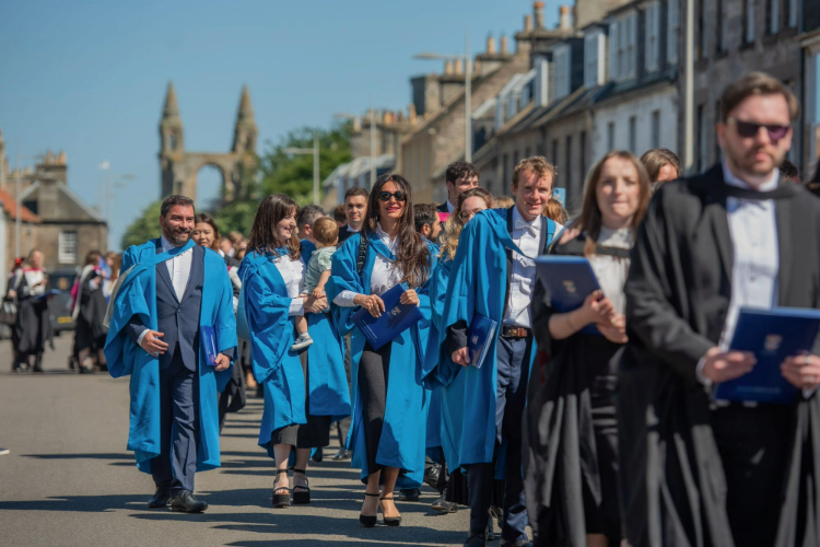 St Andrews PhD graduates, dressed in blue gowns, process down North Street in the sun